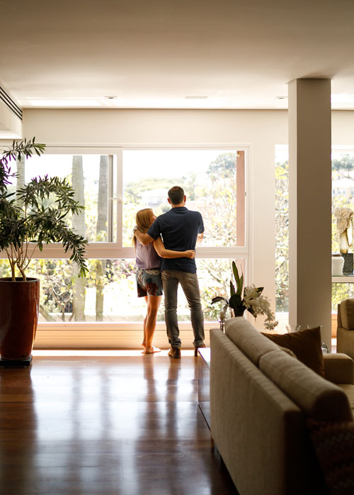Photo of couple standing in front of a window | Featured image for Mackay Conveyancing Location Page by Map Lawyers.